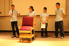 Students presenting behind wooden chair with red cushions